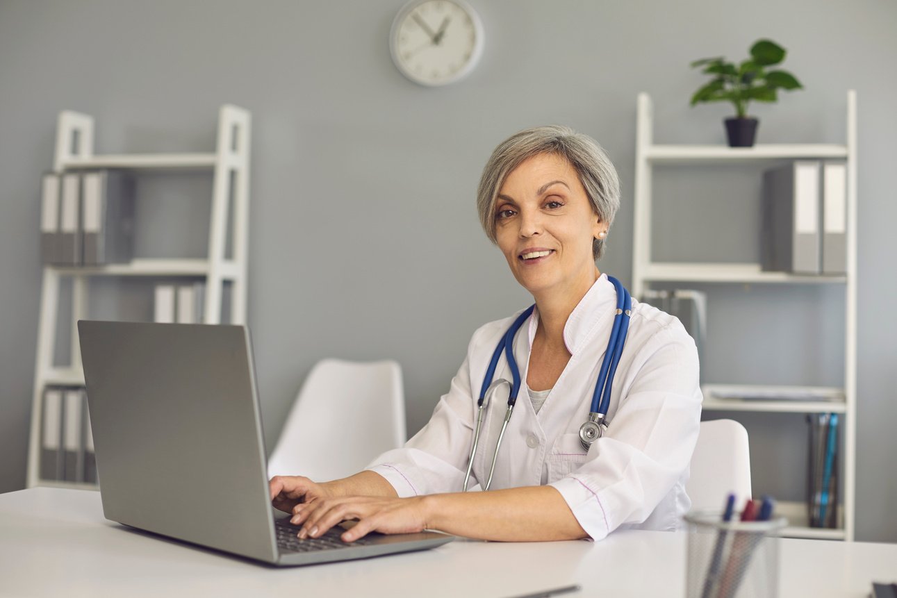 Portert Positive Matrue Doctor Woman with Laptop in Clinic Office. Doctor Online.